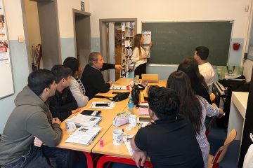 Kinga writing words in French on a blackboard during a French course, the students listen to her attentively.