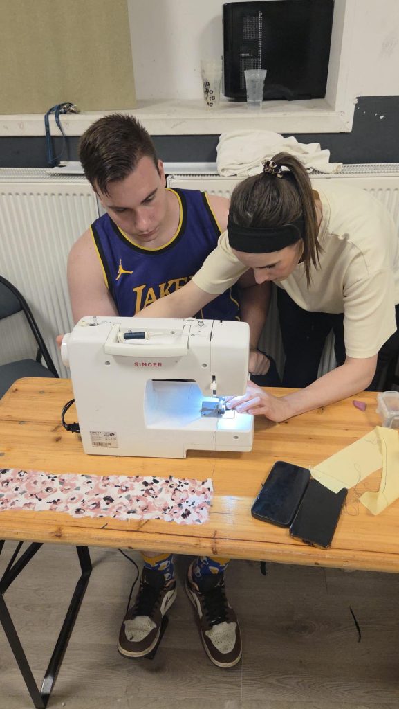 Silviu learning how to use a sewing machine - a person is showing him